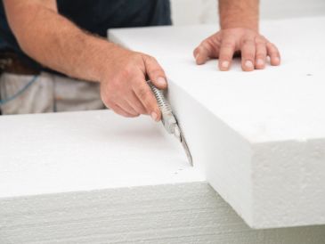 Person cutting a white foam board with a utility knife.
