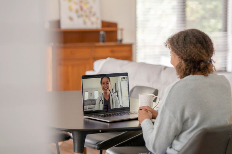 A female patent of African decent meets with her doctor remotely via a video call.