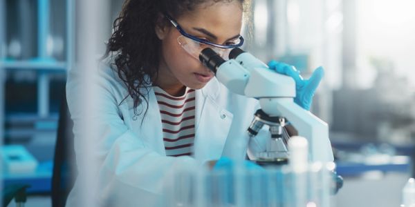 Female scientist examining samples through a microscope in a lab.