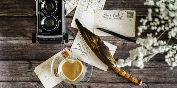 Vintage camera, old letters, quill pen, and coffee on wooden table.