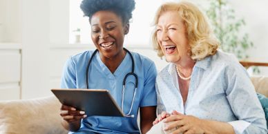 Nurse and elderly woman happily using a tablet.