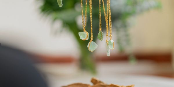 Delicate green stone pendants hanging on gold chains with a blurred natural background.