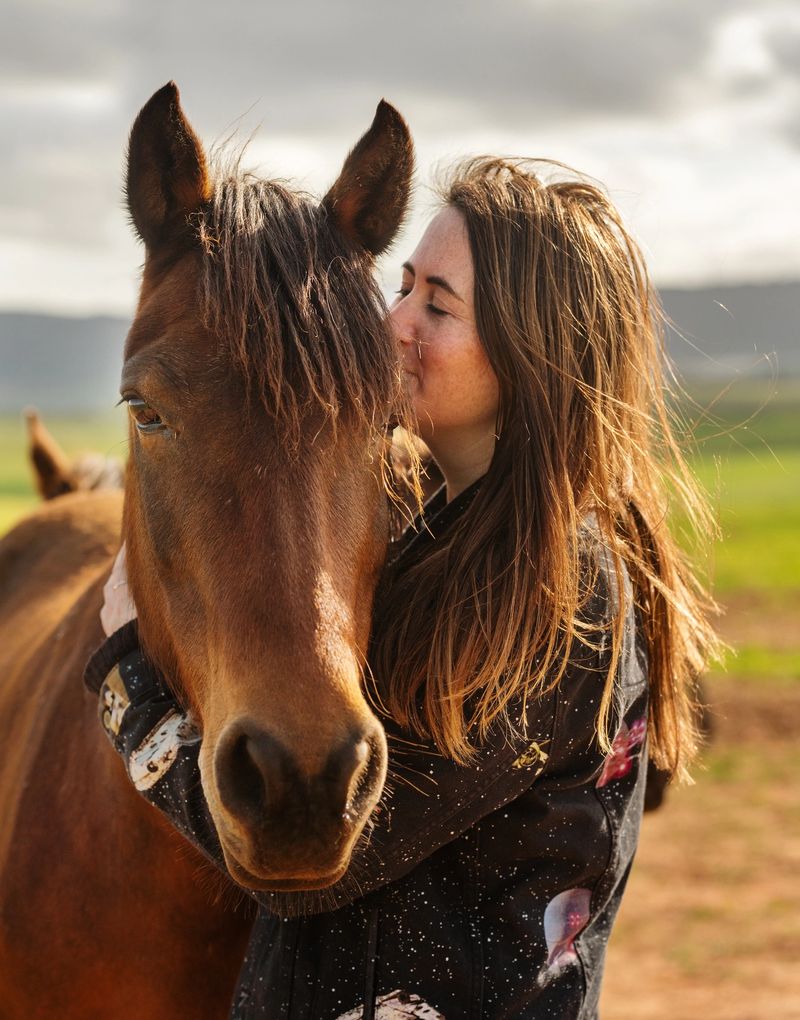 Female farmer kissing her horse while standing together in a pasture on a farm in the morning