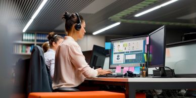 Woman working at dual monitors with headset in office.