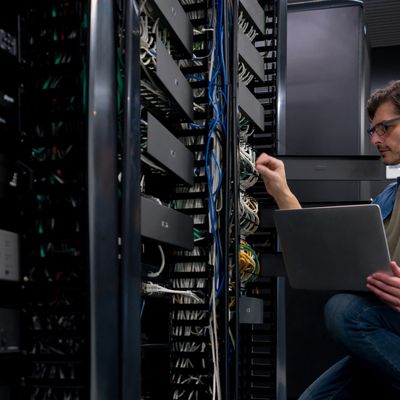 Technician working on server racks with a laptop in a data center.