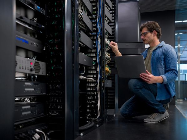 Technician working on server racks with a laptop in a data center.