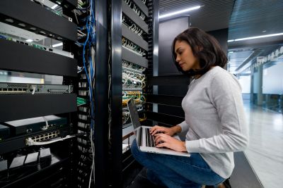 Woman working on laptop in a server room.