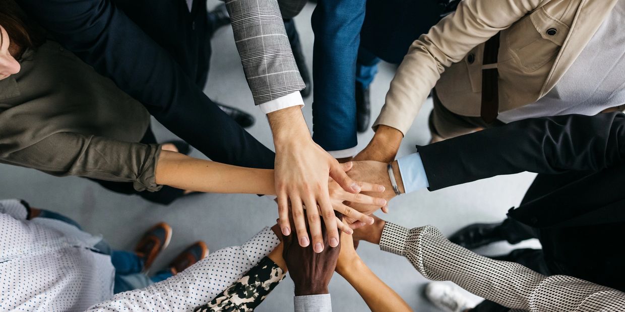 Diverse group joining hands in a team huddle, symbolizing unity and collaboration.