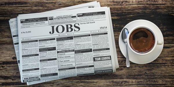 Newspaper job listings with a cup of coffee on a wooden table.