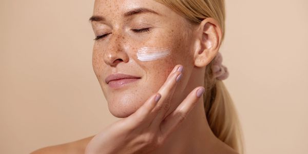 Woman with blonde hair putting anti-aging medication on her face.