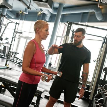 Woman lifting dumbbells with trainer guidance in gym.