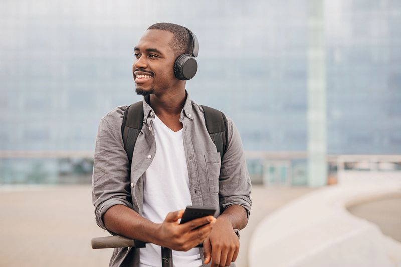 One man, young black male on electric scooter and using smart phone in city.