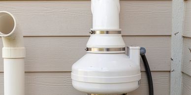 White PVC pipes and an electrical box on beige house siding.
