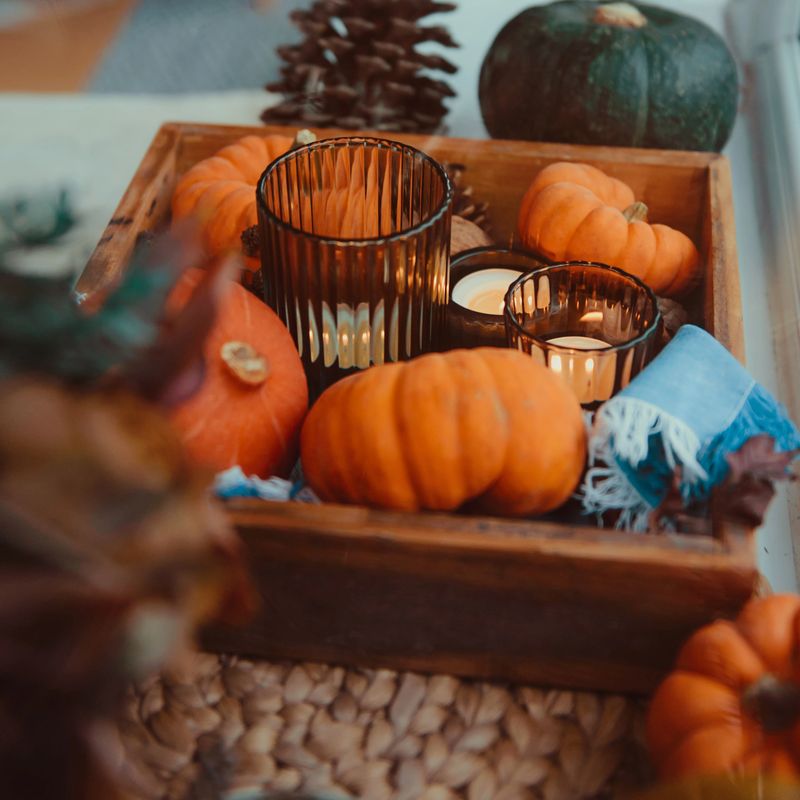 Close up autumn cozy mood composition on the windowsill. Pumpkins, cones, candles on wooden tray. Autumn, fall, thanksgiving hygge home decor. Square card. Selective focus. Copy space