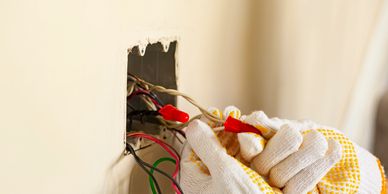 Electrician working on exposed wires inside a wall outlet.