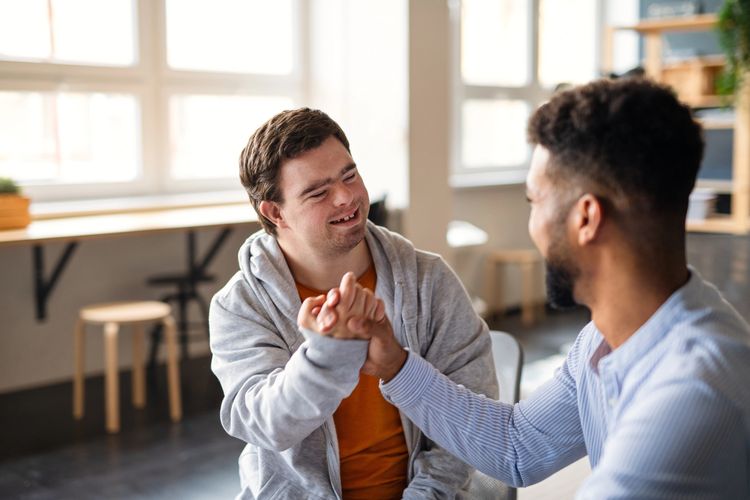 Two men smiling and shaking hands in a bright room.