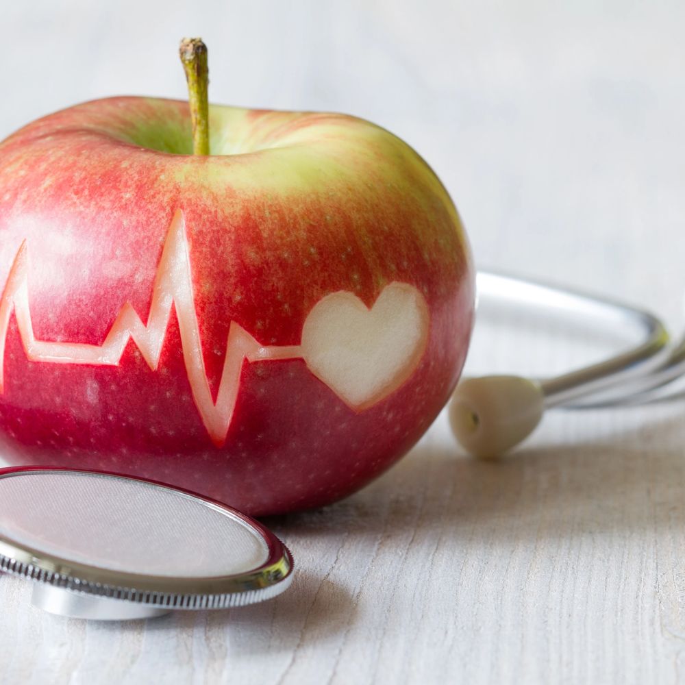 Apple with heart and heartbeat carved, next to a stethoscope.