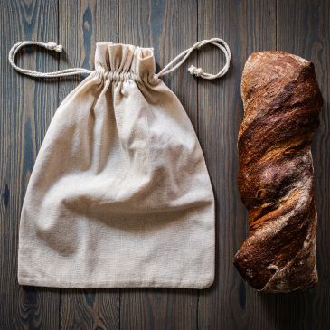 Cloth bag and rustic loaf of bread on wooden surface.