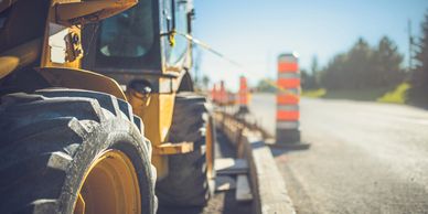Close-up of a yellow construction vehicle near traffic safety cones on a sunny day.
