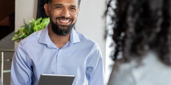 Man smiling and holding a tablet during a conversation.