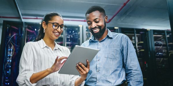 Two professionals smiling and looking at a tablet.