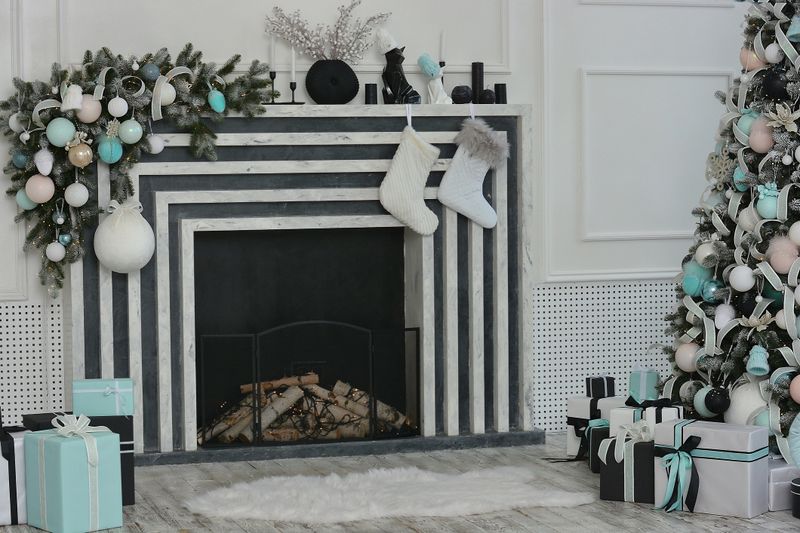 Festive Christmas interior. The Christmas tree with boxes of gifts is beautifully decorated with decorations. Beautiful Cfireplace with a Christmas composition of branches of a tree, balls, boots