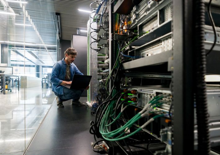 Technician working on server racks with a laptop in a modern data center.