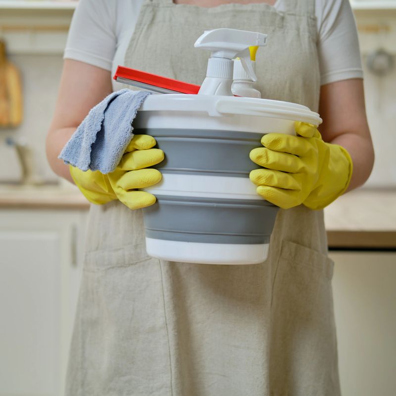 A woman with a bucket and a rag while cleaning in the home kitchen, a housewife is doing household chores