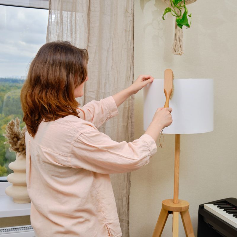 Woman brushing dust from floor lamp in home living room