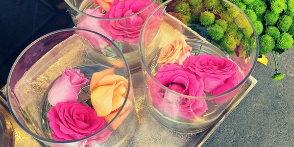Three glass cups with floating pink and peach roses on a metallic tray beside green chrysanthemums.
