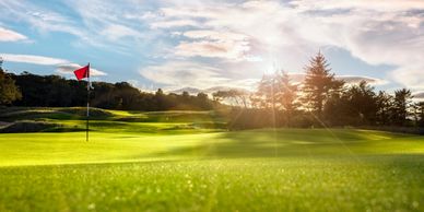 Sunlight shines on a golf course green with a red flag on the hole.