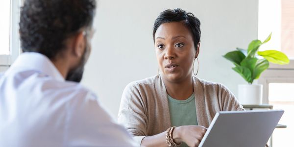 A woman attentively discussing something with a man across a laptop.