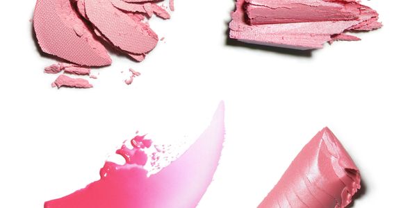 Various crushed and smeared pink makeup products on white background.