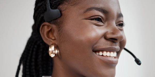 Smiling woman with braided hair wearing a headset and gold earrings.