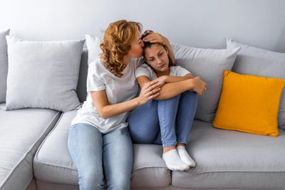 A woman comforting a distressed teenage girl on a couch.