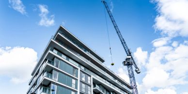 Modern residential building under construction with a crane against a bright blue sky.