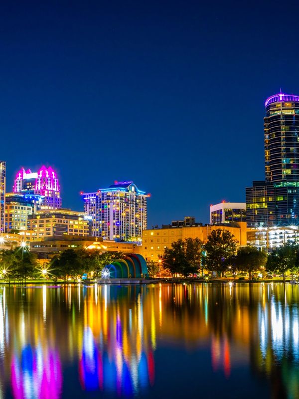 City skyline at night reflecting colorful lights on water.