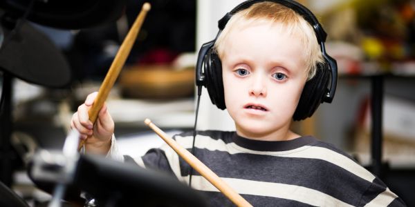 Young boy playing drums with headphones.