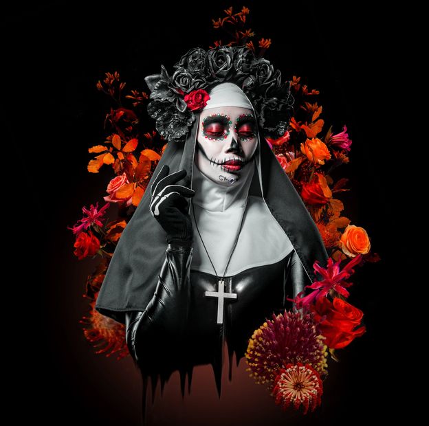 A woman dressed as a Day of the Dead nun with floral makeup and a crown of black and red flowers.