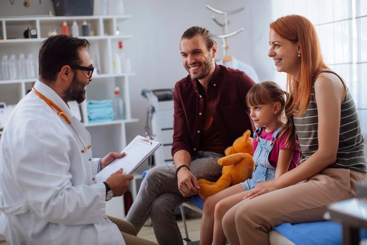 Family consulting a doctor with a young girl holding a teddy bear.