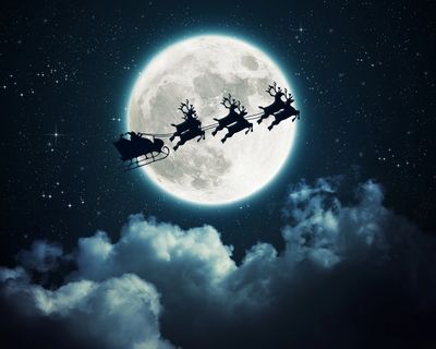 Silhouette of Santa's sleigh and reindeer flying across a full moon.