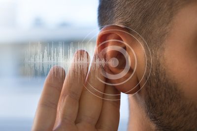 An ear with a target icon symbol, a hand holding the ear as if intent to listen.