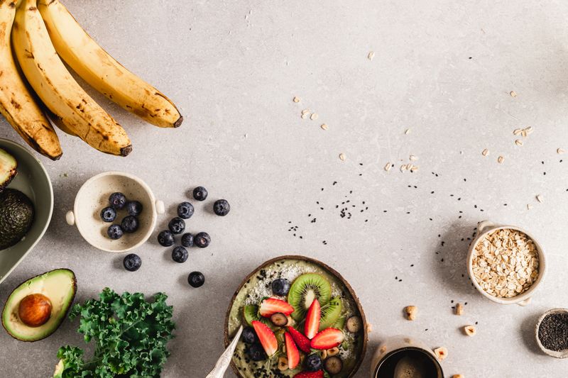 Directly above shot of smoothie bowl with banana, kiwi, strawberries, blueberries, avocado, oats, black sesame seeds over kitchen counter. Healthy fruit smoothie bowl with copy space.