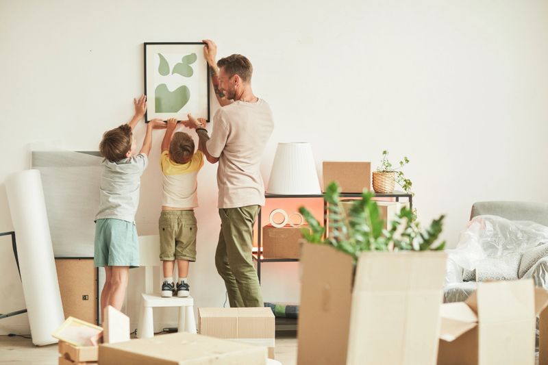 Father with two sons hanging pictures on wall while moving in to new home