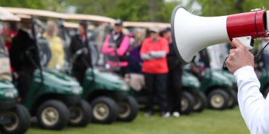 Person with megaphone addressing a group near golf carts.