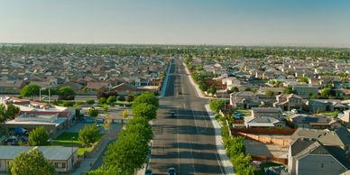 A wide suburban street stretches through a neighborhood of houses under a clear blue sky.