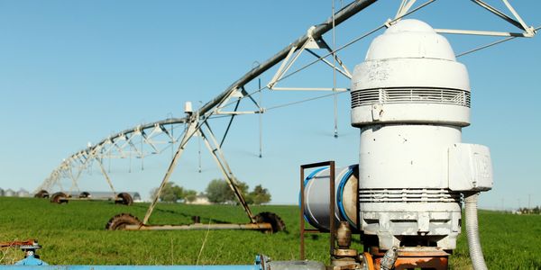 Irrigation system on a green farm field under clear blue sky.