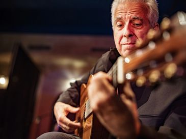 An elderly man playing an acoustic guitar with focus and emotion.