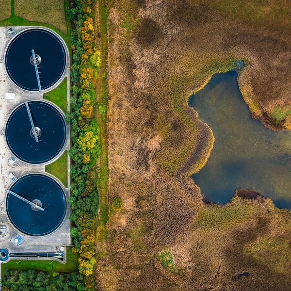 Aerial view of circular water treatment tanks next to a marshy wetland area.