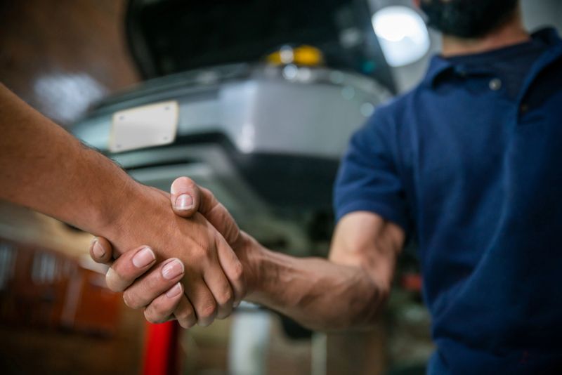 Unrecognizable customer and supervisor at an auto repair shop shaking hands after fixing the car very successfully - Automobile industry concepts